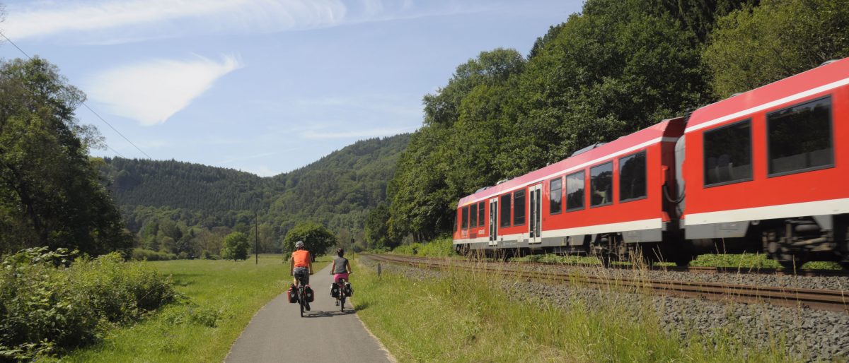 Radweg mit zwei Radfahrern und rotem Zug am Bildrand