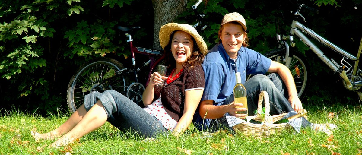 Lachendes Pärchen im Gras vor Fahrrädern mit Picknickkorb